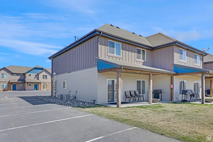 Back of property with uncovered parking, board and batten siding, a lawn, roof with shingles, and a residential view