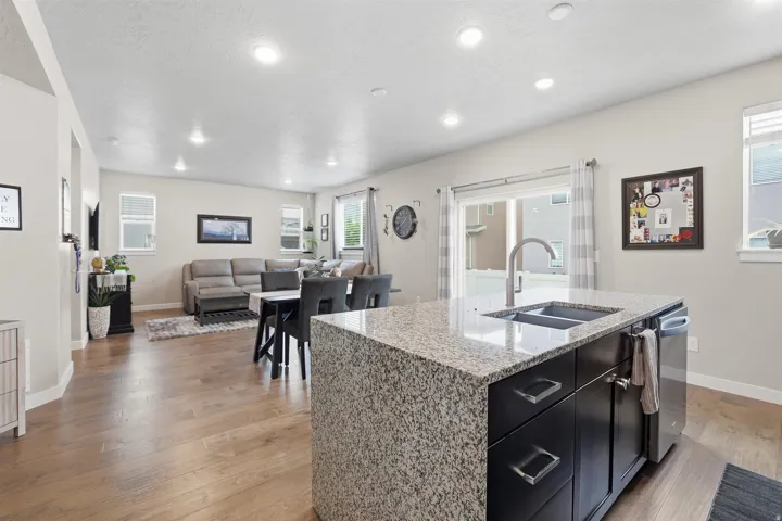 Kitchen featuring dark cabinets, light stone countertops, a center island with sink, light wood-type flooring, and open floor plan