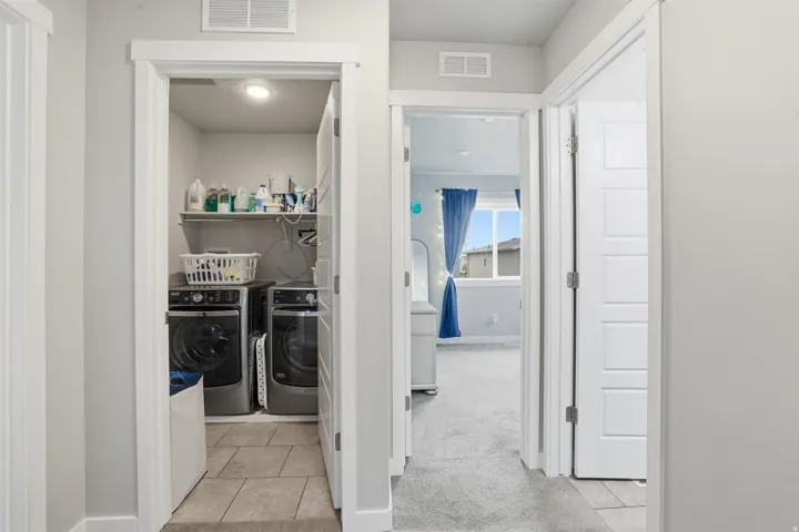 Laundry room featuring light colored carpet, washing machine and clothes dryer, and light tile patterned flooring
