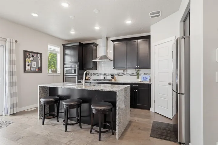 Kitchen featuring light stone counters, stainless steel appliances, an island with sink, light wood-style flooring, and recessed lighting