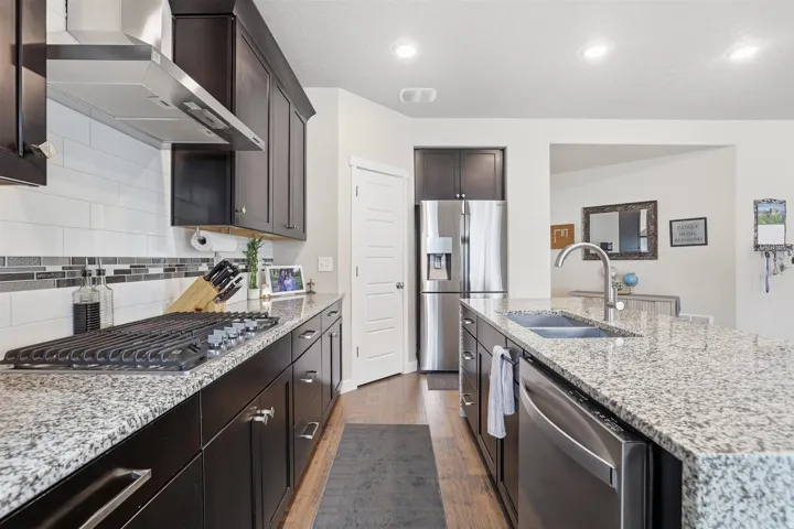 Kitchen with light stone countertops, dark wood-style floors, stainless steel appliances, dark wood finish cabinetry, and decorative backsplash
