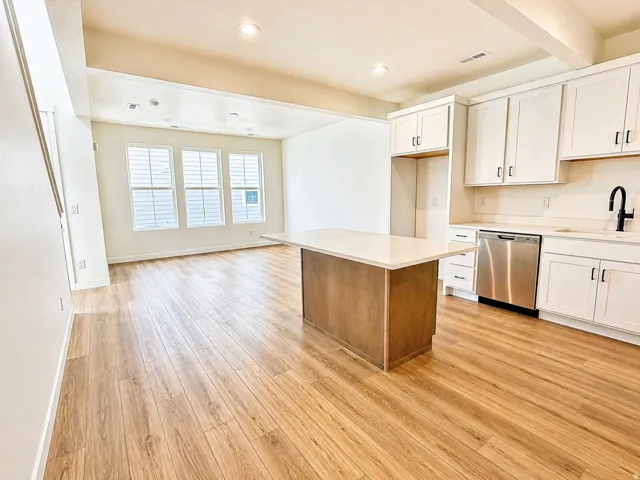 Two tone kitchen with light countertops, open floor plan, light wood finished floors, dishwasher, and a kitchen island