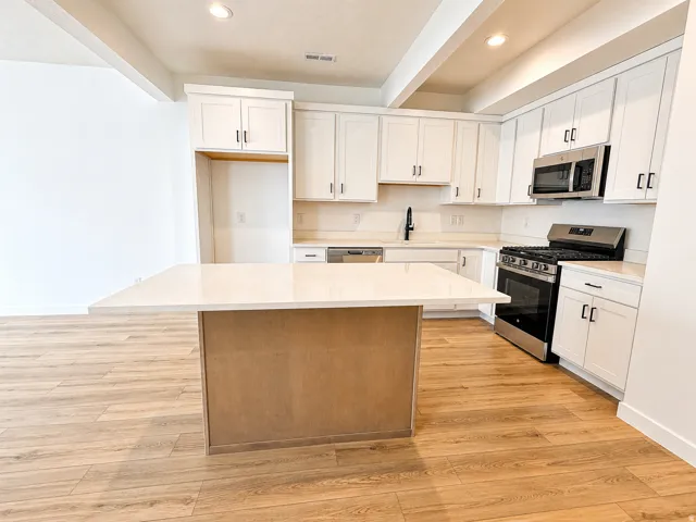 Dual tone kitchen with stainless steel appliances, a center island, light wood finished floors, beam ceiling, and recessed lighting