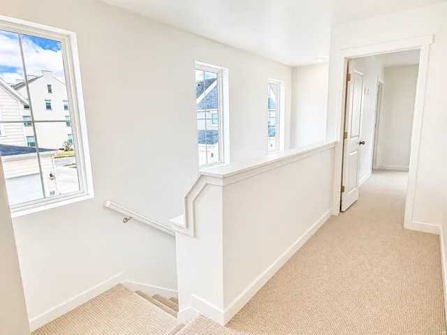 Hallway with light colored carpet and an upstairs landing