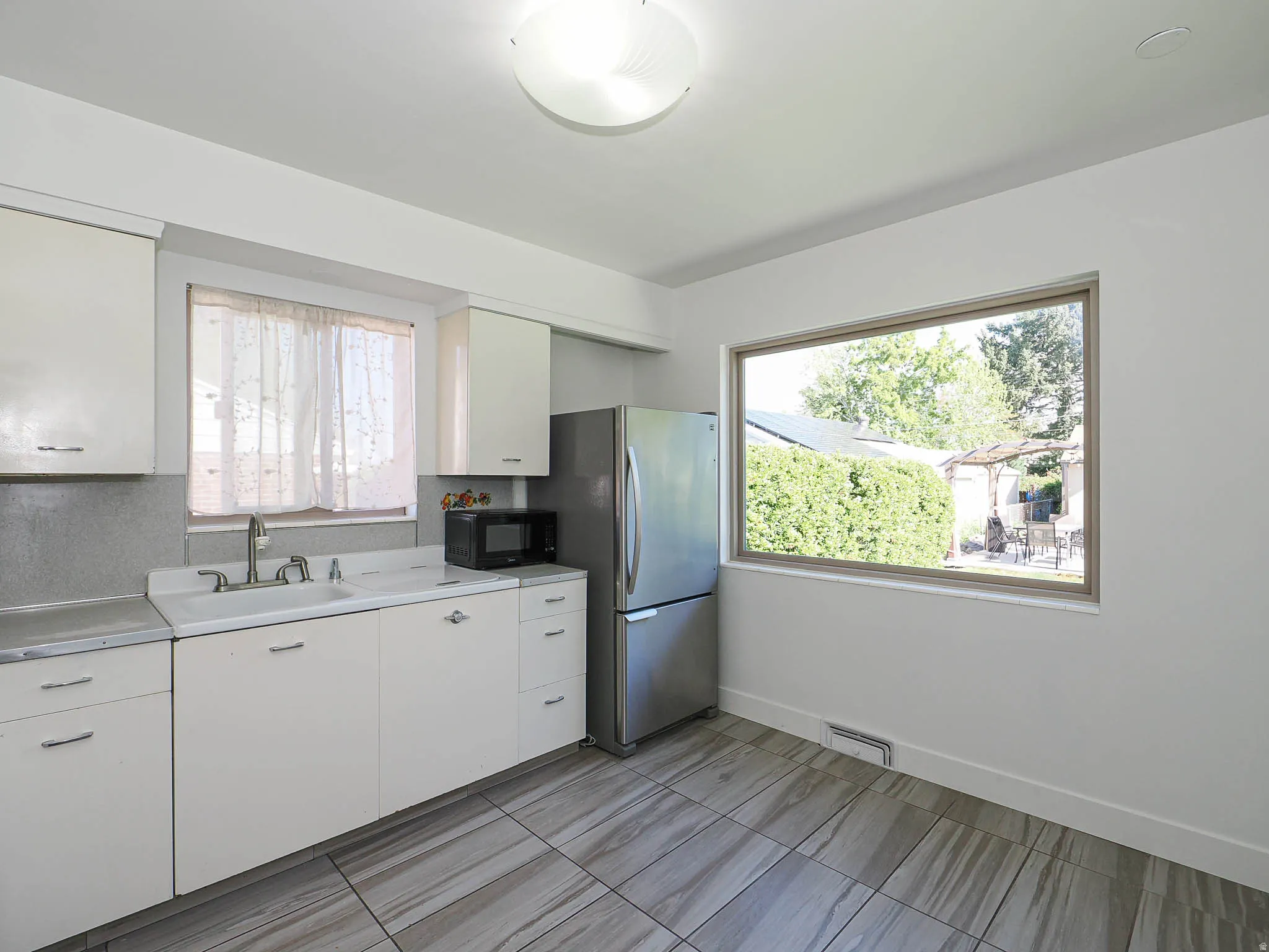 Kitchen with light countertops, freestanding refrigerator, white cabinets, and black microwave