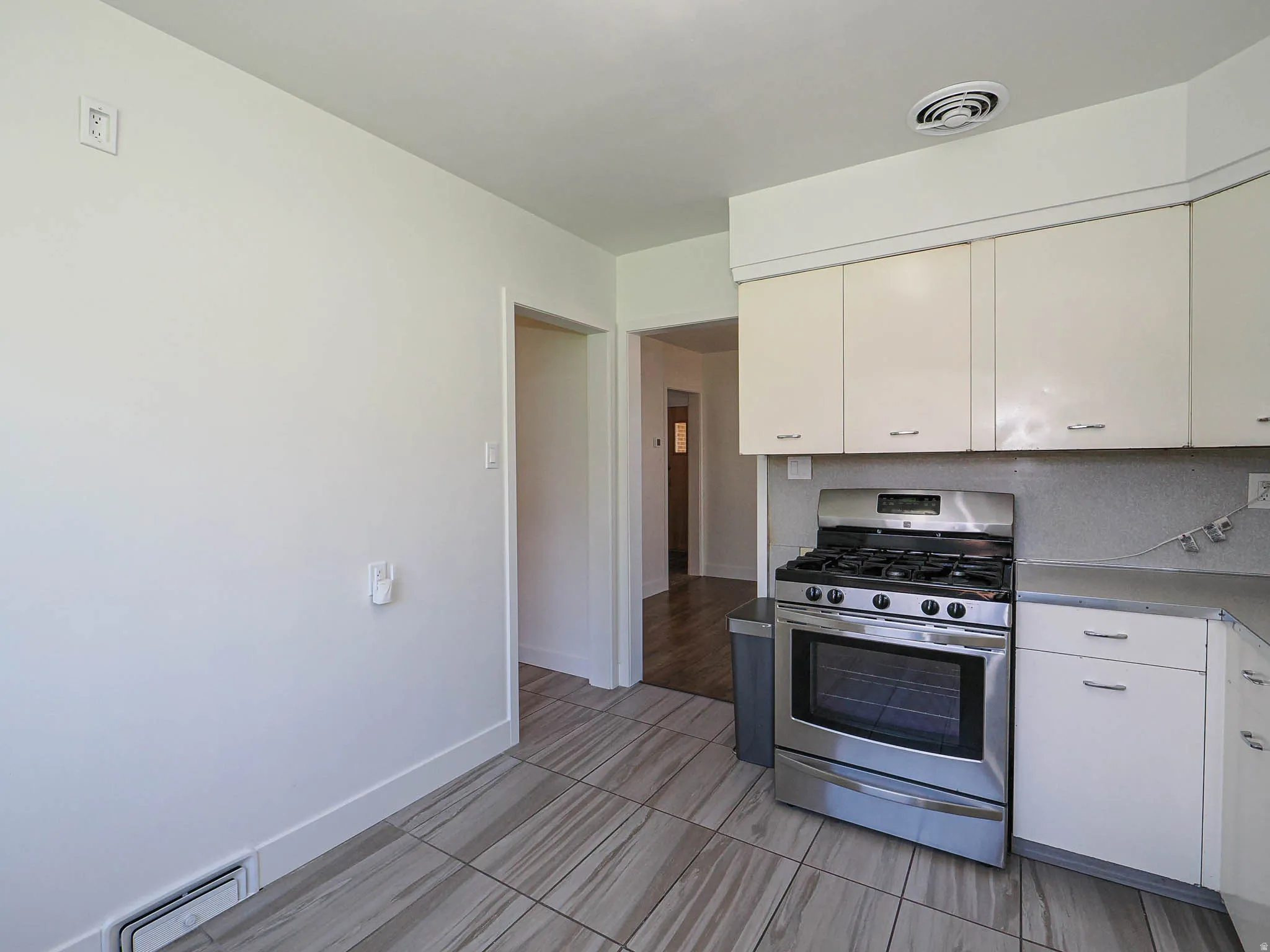 Kitchen featuring stainless steel gas range oven, light countertops, a baseboard heating unit, and white cabinets