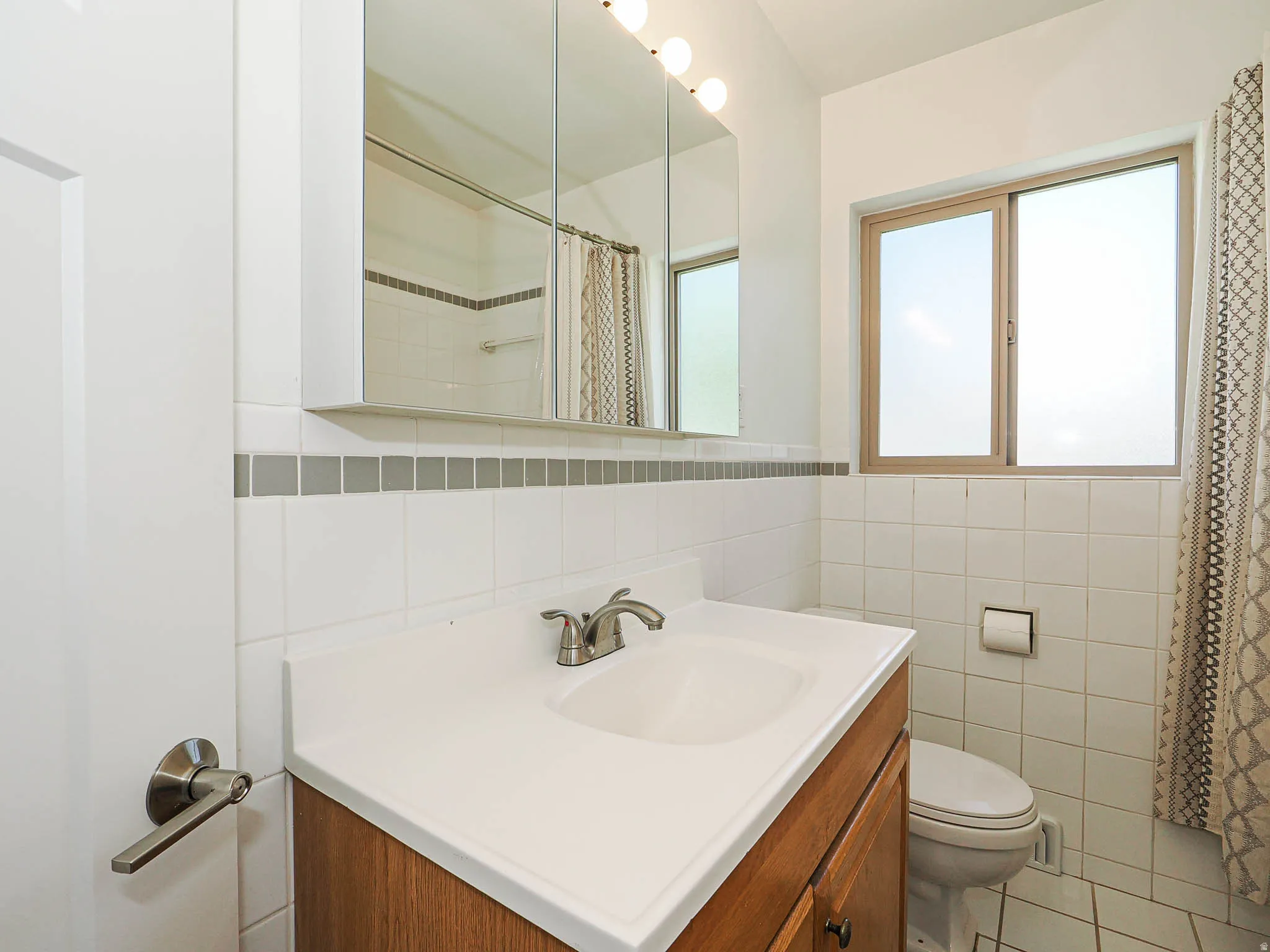 Bathroom featuring a shower with curtain, vanity, tile walls, a wainscoted wall, and light tile patterned floors