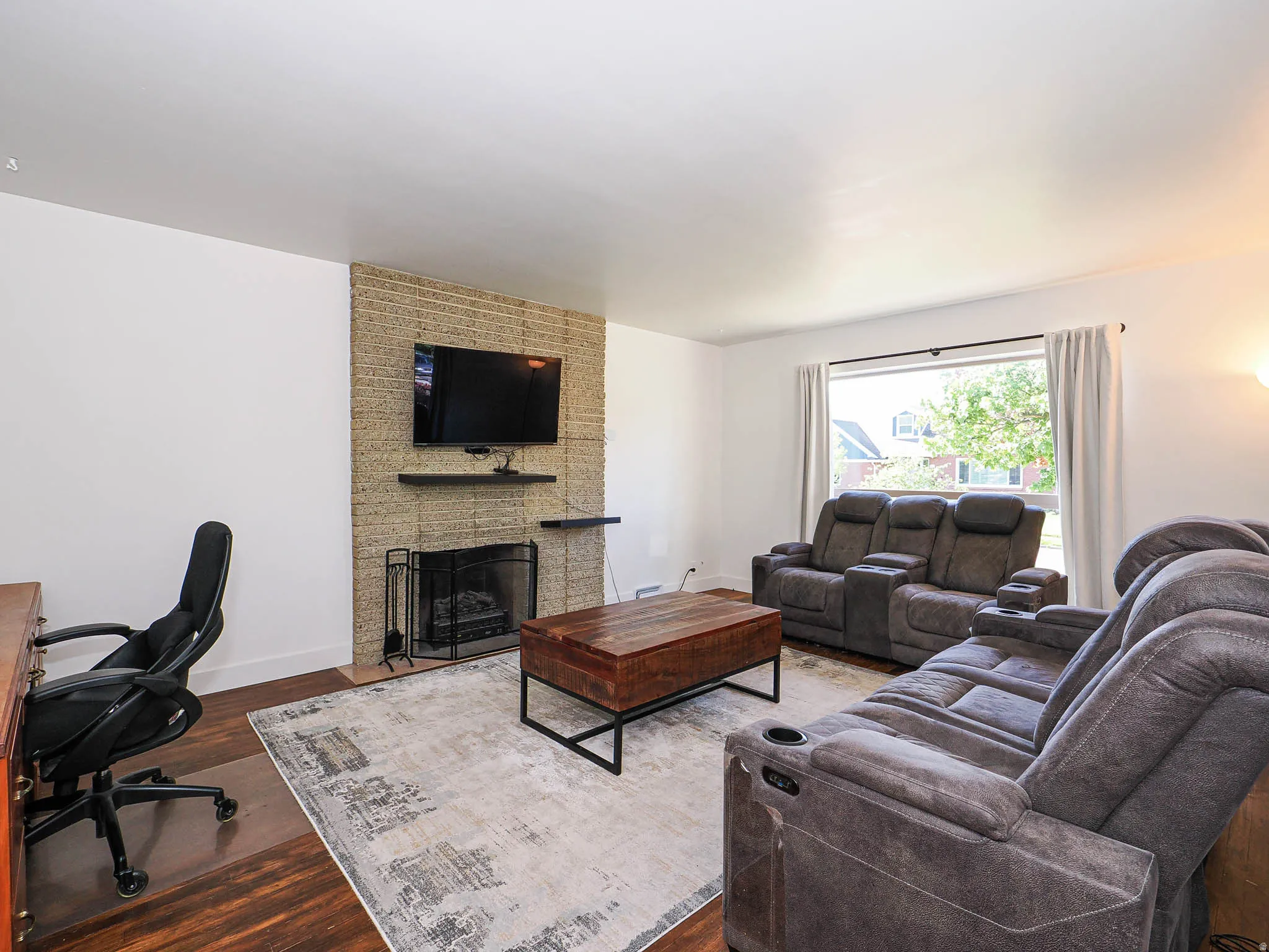 Living area with a large fireplace, dark wood-style flooring, and a desk