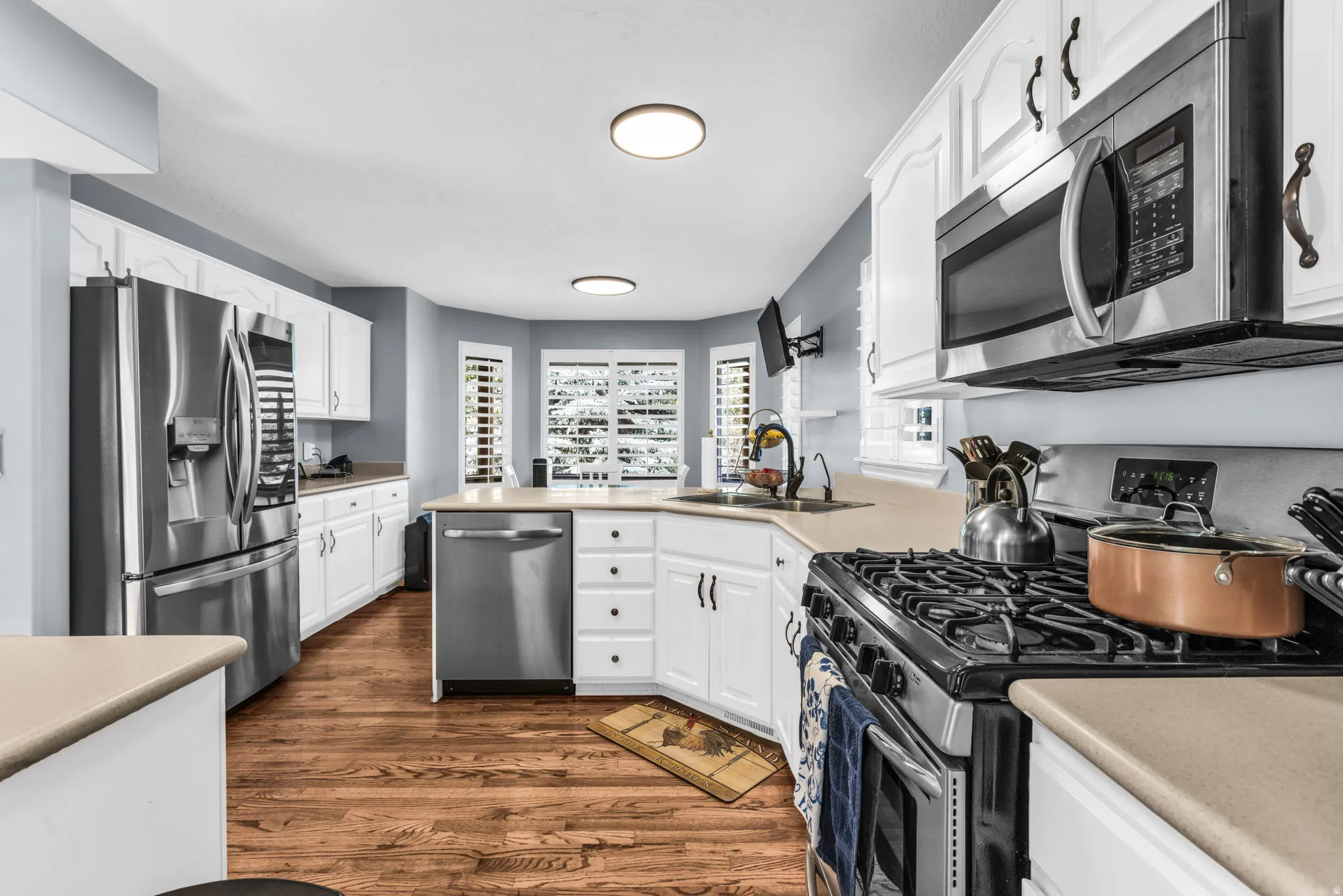 Kitchen featuring white cabinetry, stainless steel appliances, wood-finish flooring, light-toned countertops, and multiple windows