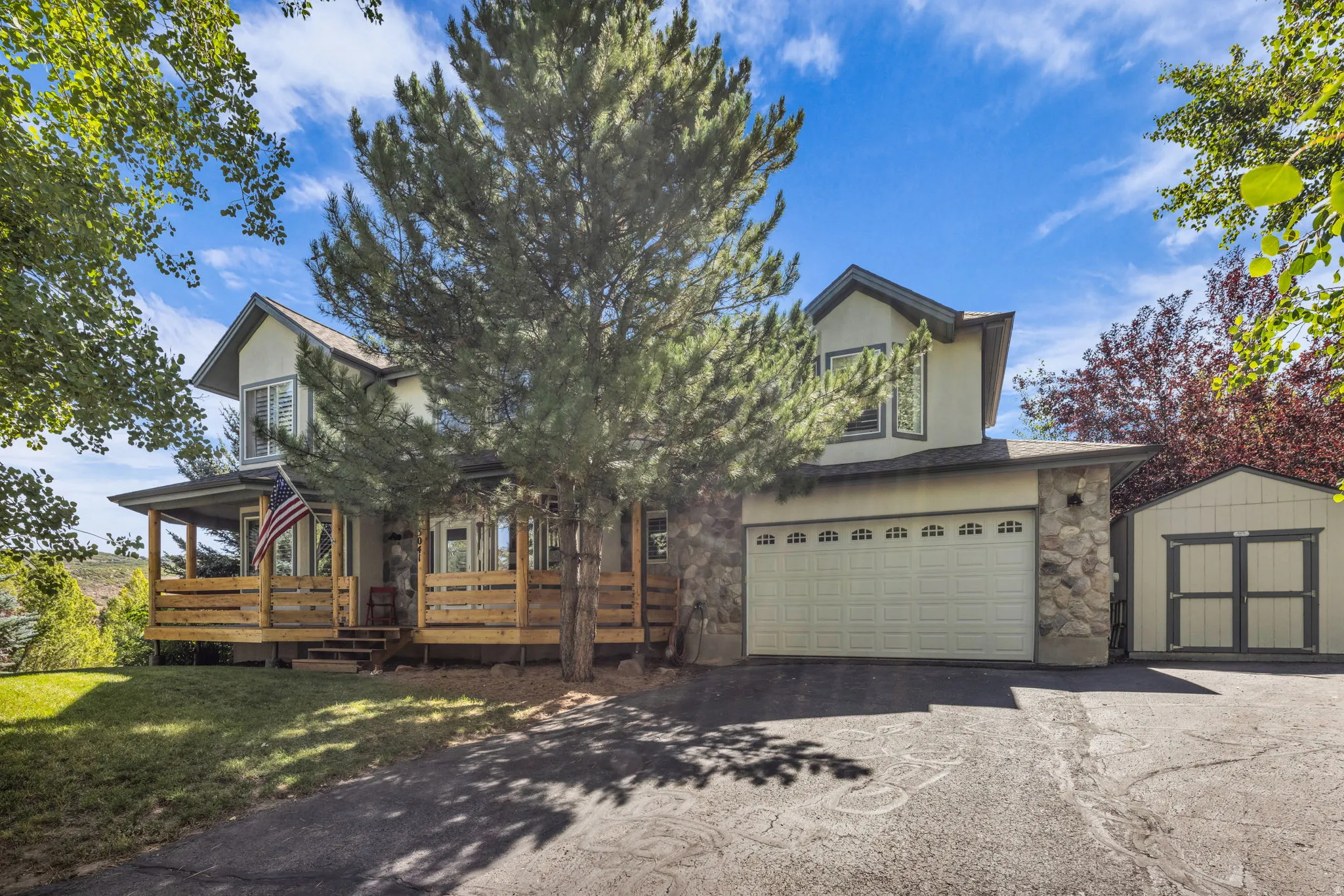 Two-story exterior with stone and stucco finishes, attached two-car garage, expansive wood deck, and separate storage shed