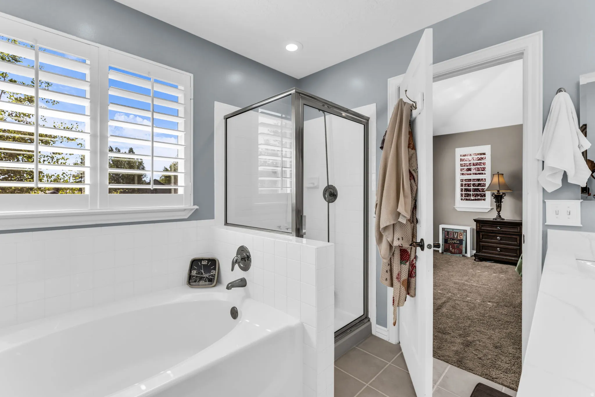 Built-in soaking tub with white subway tile surround, plantation shutters, and a glass-enclosed shower
