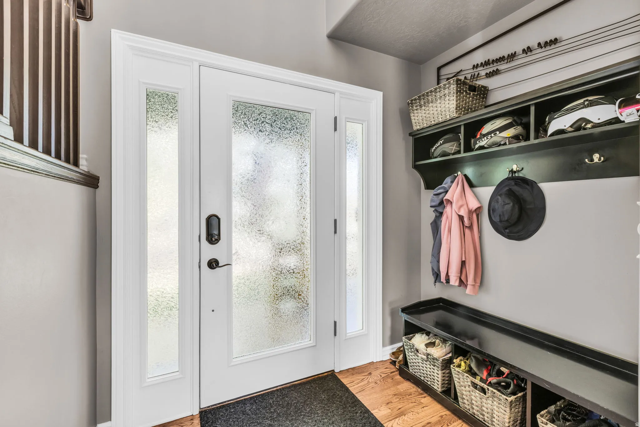 Entryway featuring a white door with frosted glass, wood-finish flooring, and a built-in dark wood storage bench with shelving and hooks