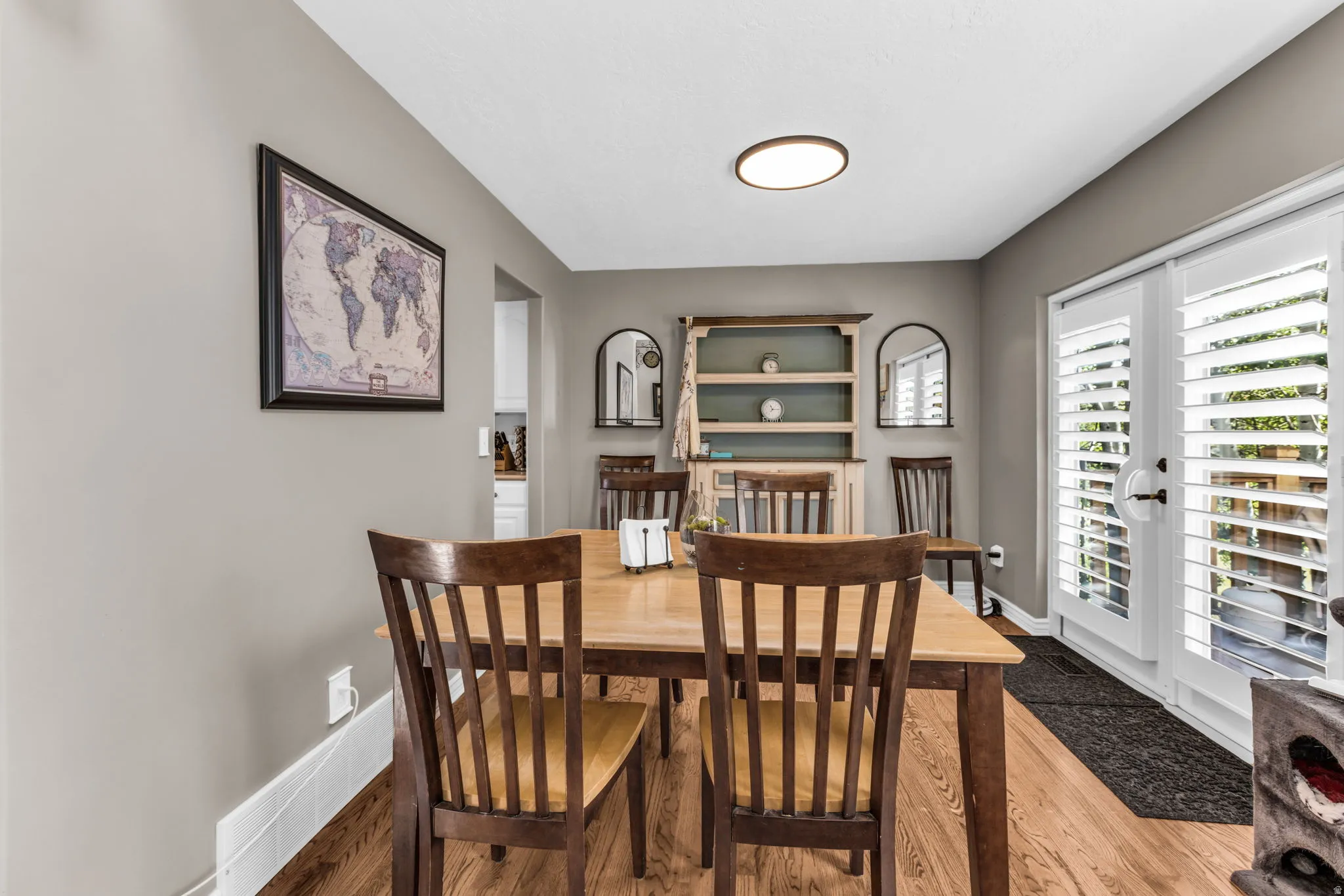 Hardwood flooring, neutral painted walls, built-in shelving, recessed lighting, and double patio doors with plantation shutters
