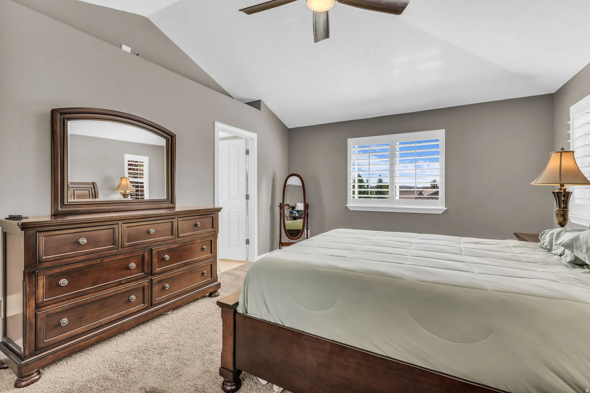 Vaulted ceiling with a ceiling fan, window with plantation shutters, and a paneled interior door