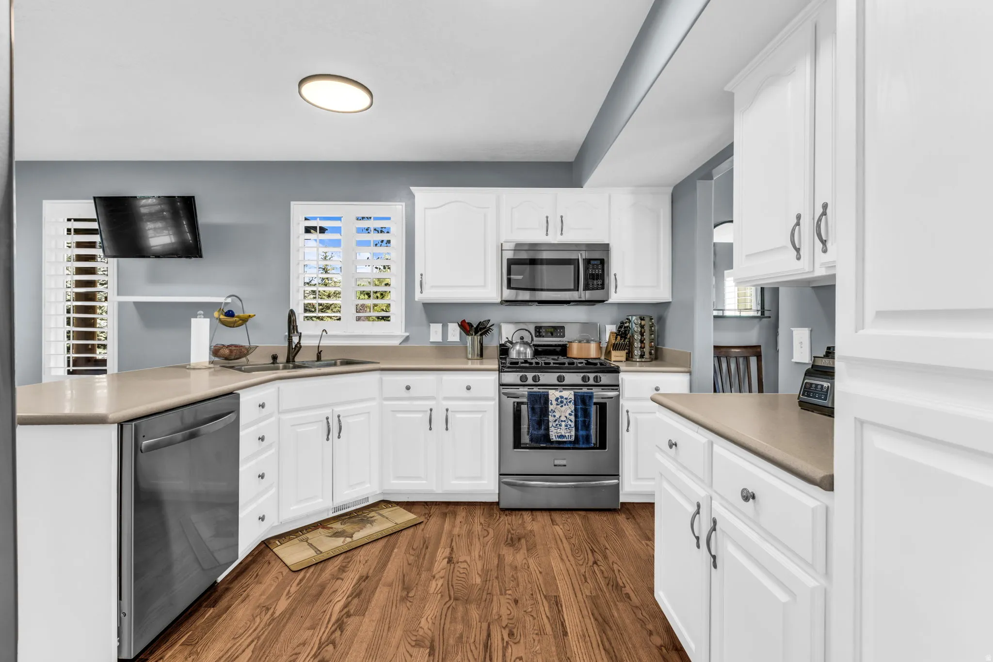 White cabinetry, stainless steel appliances, wood-finish flooring, and light-toned countertops