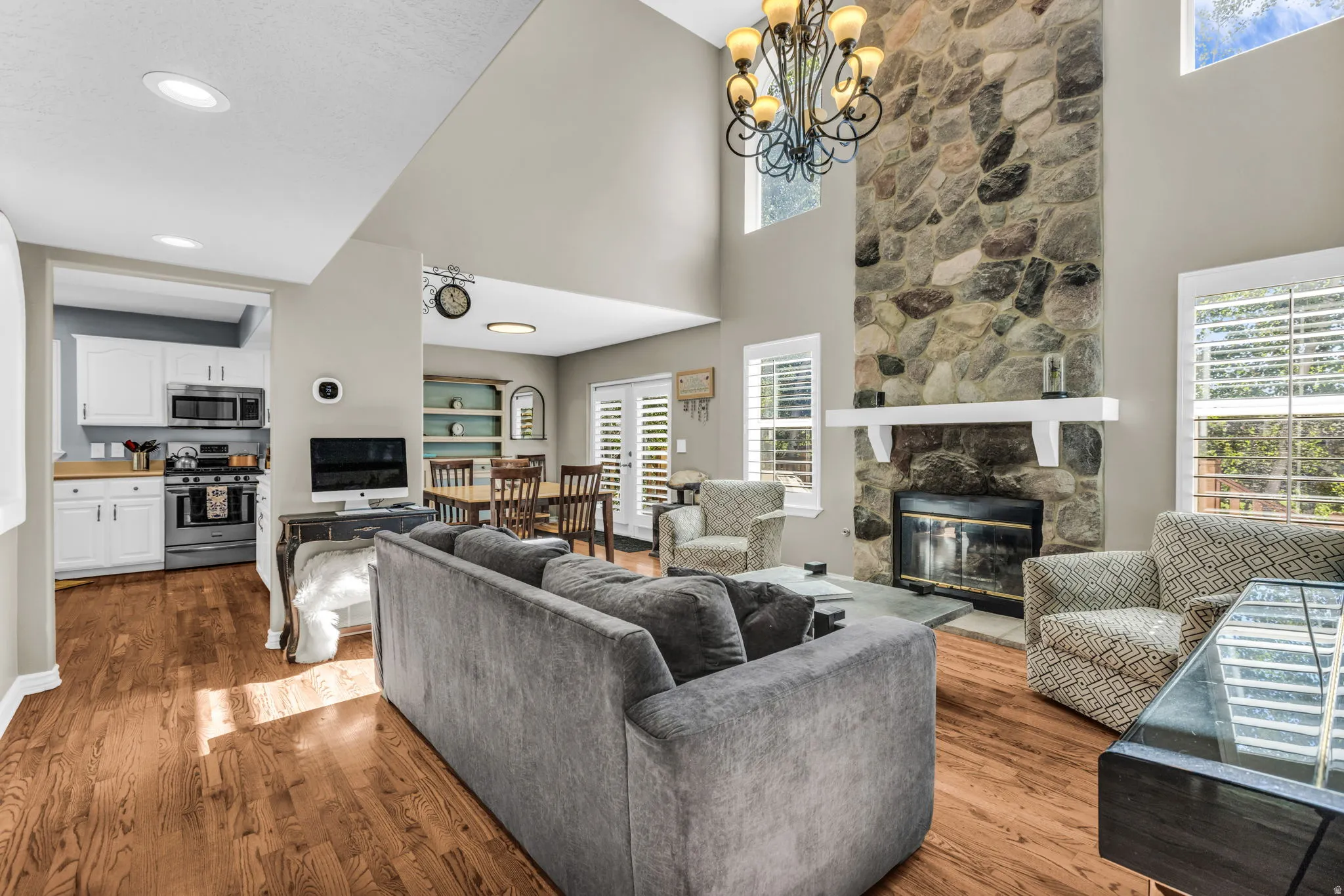 Two-story stone-clad fireplace with mantel, recessed lighting, wood-finish flooring, white cabinetry, and stainless steel appliances