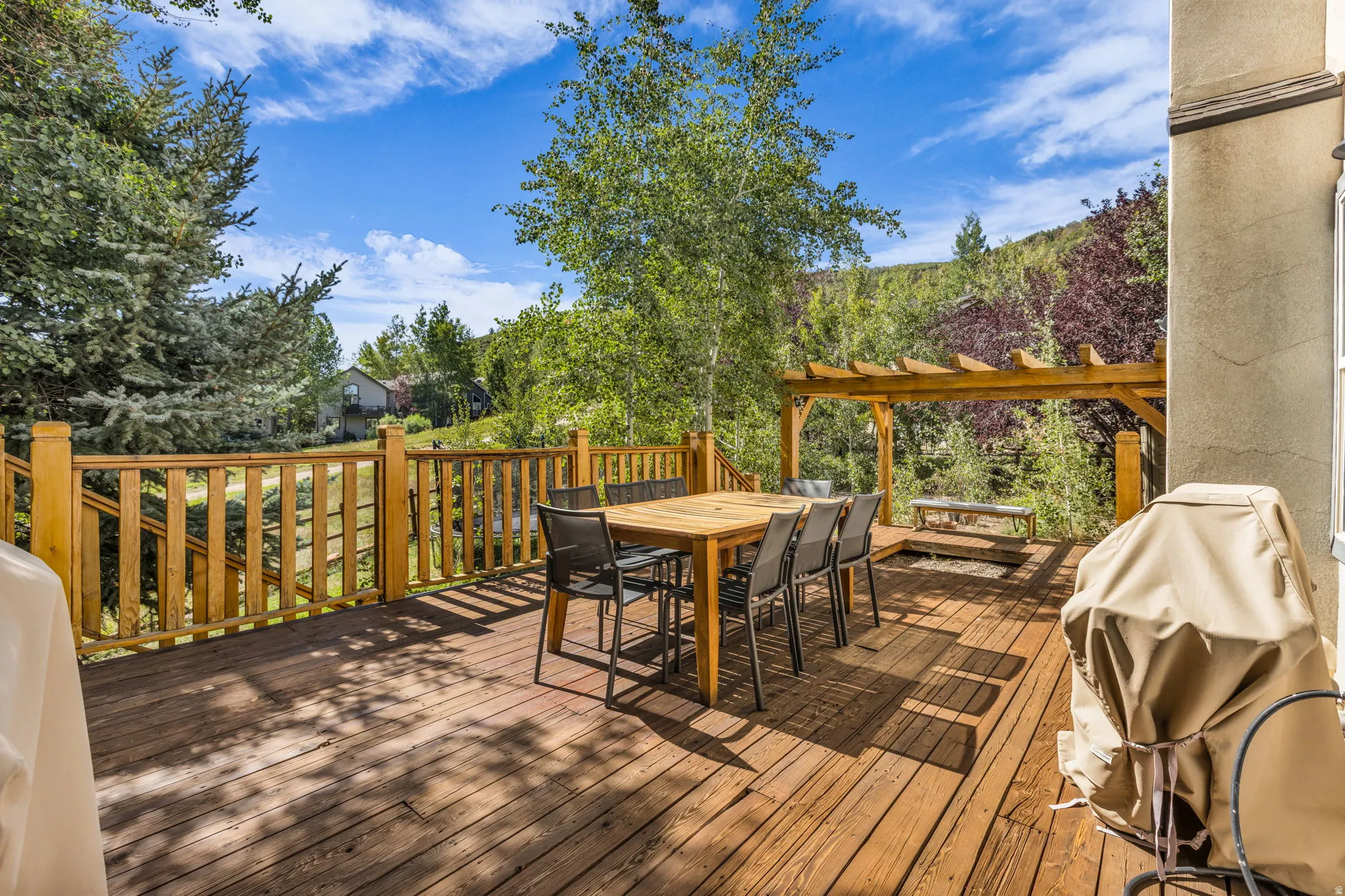 Spacious wood deck featuring a pergola, wood railing, and surrounding trees