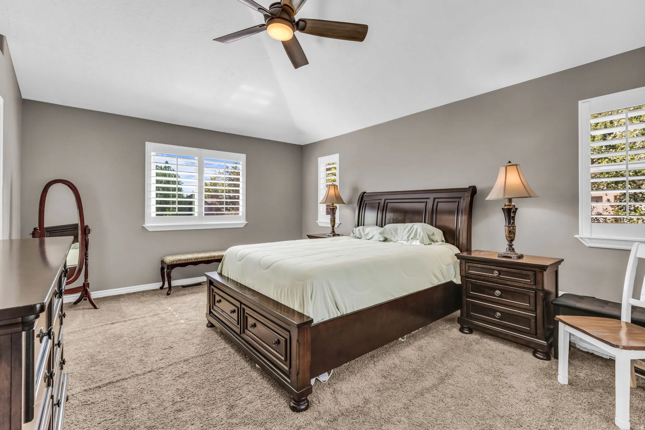 Vaulted ceiling with a ceiling fan, multiple windows with plantation shutters, and carpet flooring