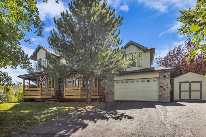 Two-story exterior with stone and stucco finishes, attached two-car garage, expansive wood deck, and separate storage shed
