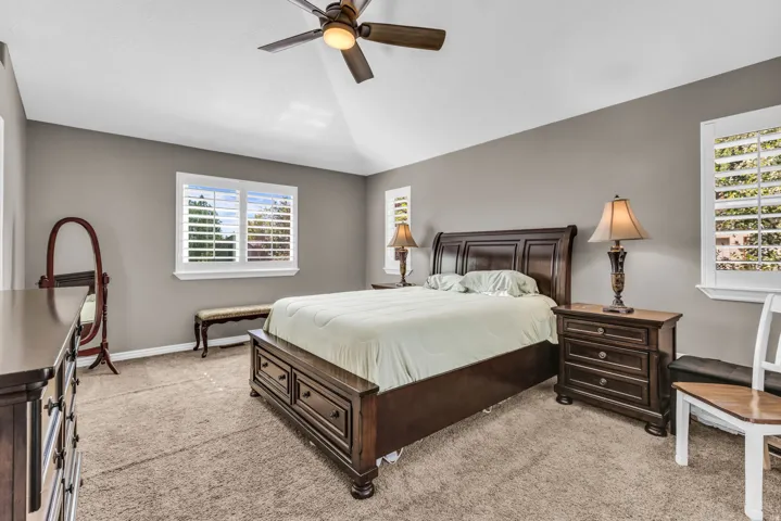 Vaulted ceiling with a ceiling fan, multiple windows with plantation shutters, and carpet flooring