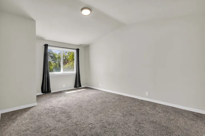 Carpeted spare room featuring baseboards and vaulted ceiling