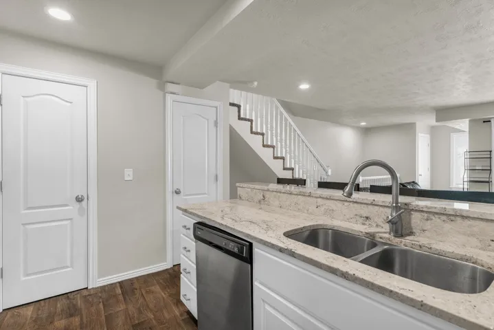 Kitchen with recessed lighting, white cabinets, light stone countertops, dark wood-style flooring, and stainless steel dishwasher