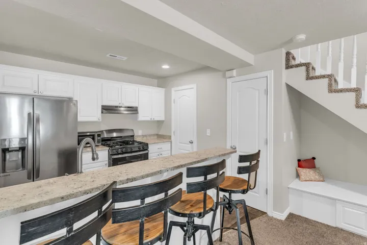 Kitchen with stainless steel appliances, white cabinetry, light stone countertops, a breakfast bar area, and recessed lighting