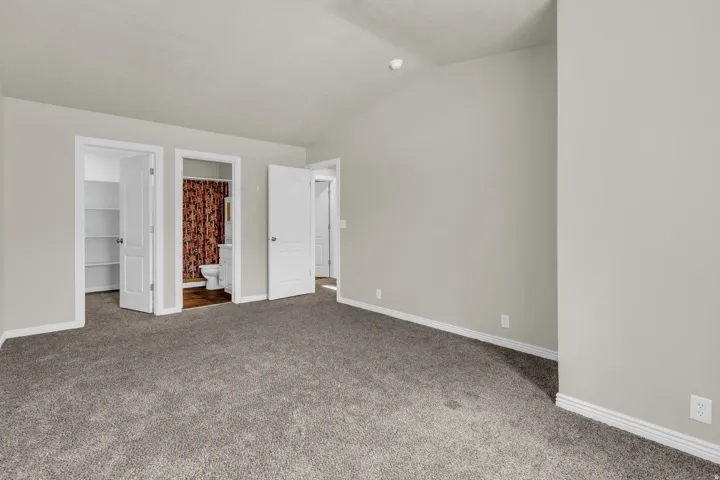 Unfurnished bedroom with a walk in closet, carpet floors, connected bathroom, and vaulted ceiling