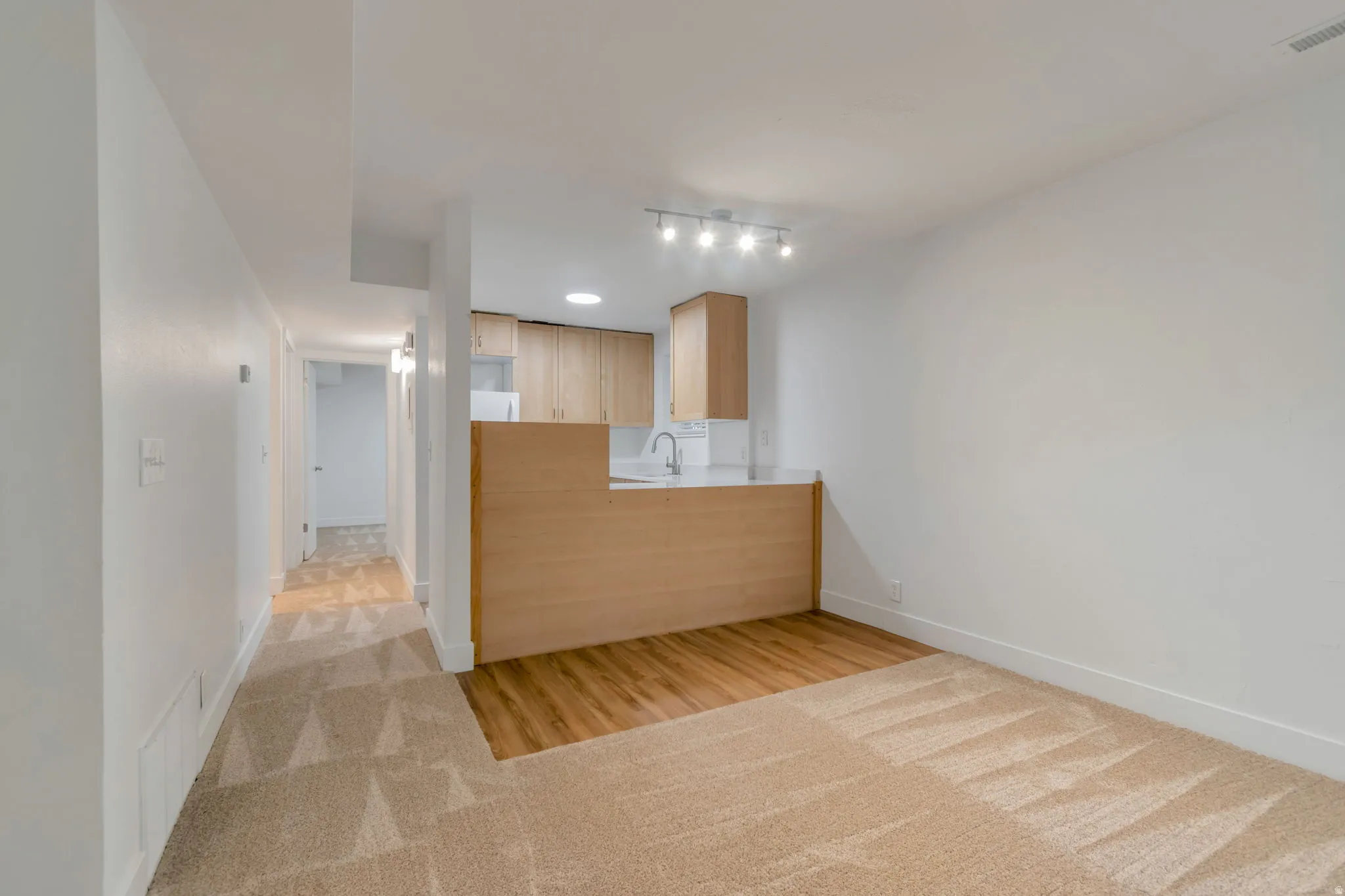 Kitchen with light countertops, light wood finish cabinetry, light wood-type flooring, and light colored carpet