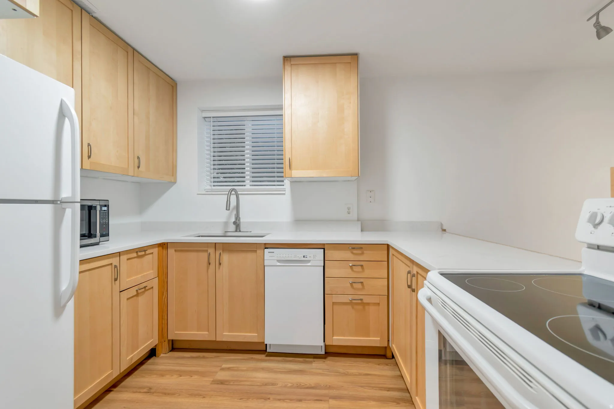 Kitchen with light wood finish cabinetry, white appliances, and light wood-type flooring
