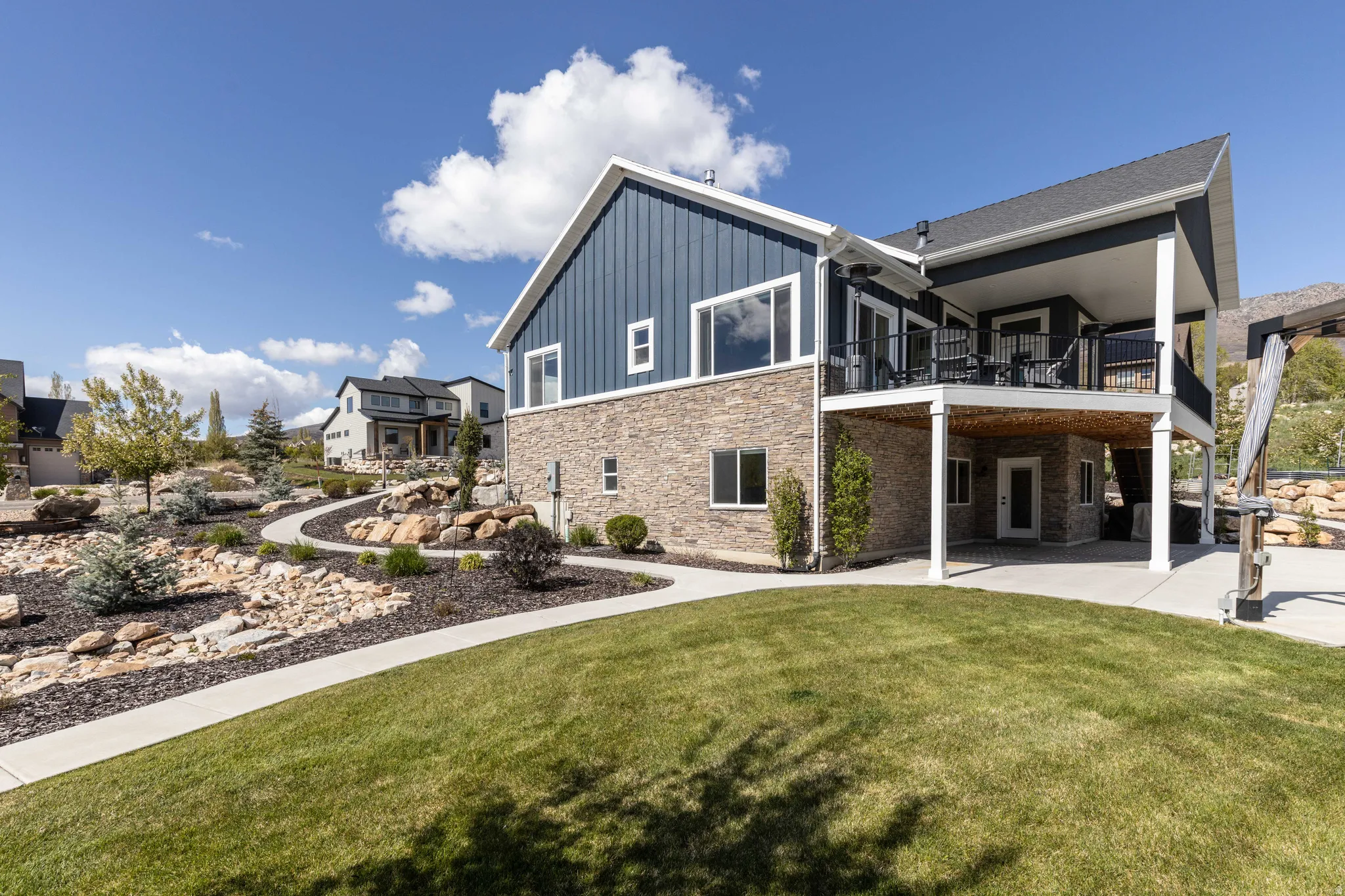 Rear view of house with board and batten siding, a yard, stone siding, a patio, and a balcony