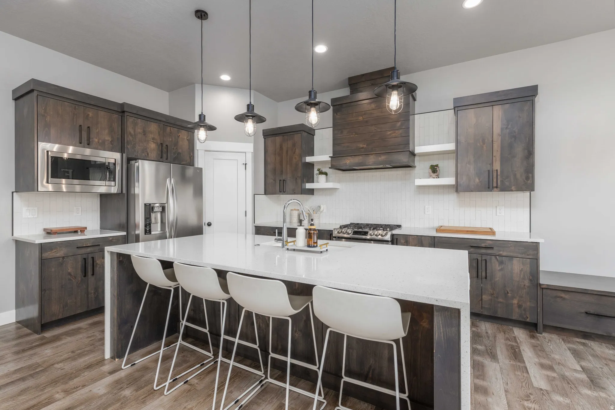 Kitchen with dark wood finish cabinetry, tasteful backsplash, light stone countertops, pendant lighting, and stainless steel appliances