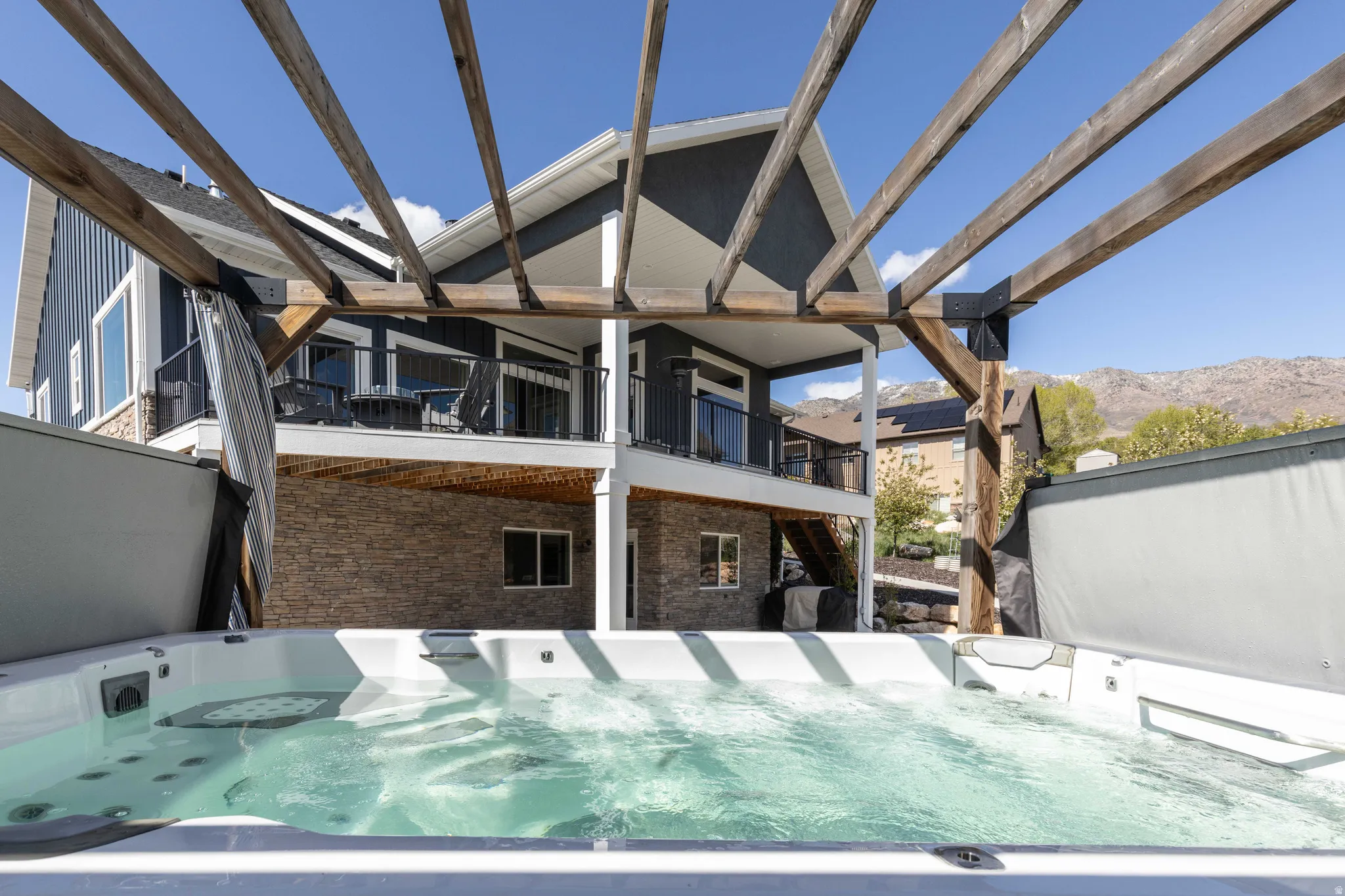 Back of house featuring brick siding, a mountain view, a hot tub, a patio area, and a balcony