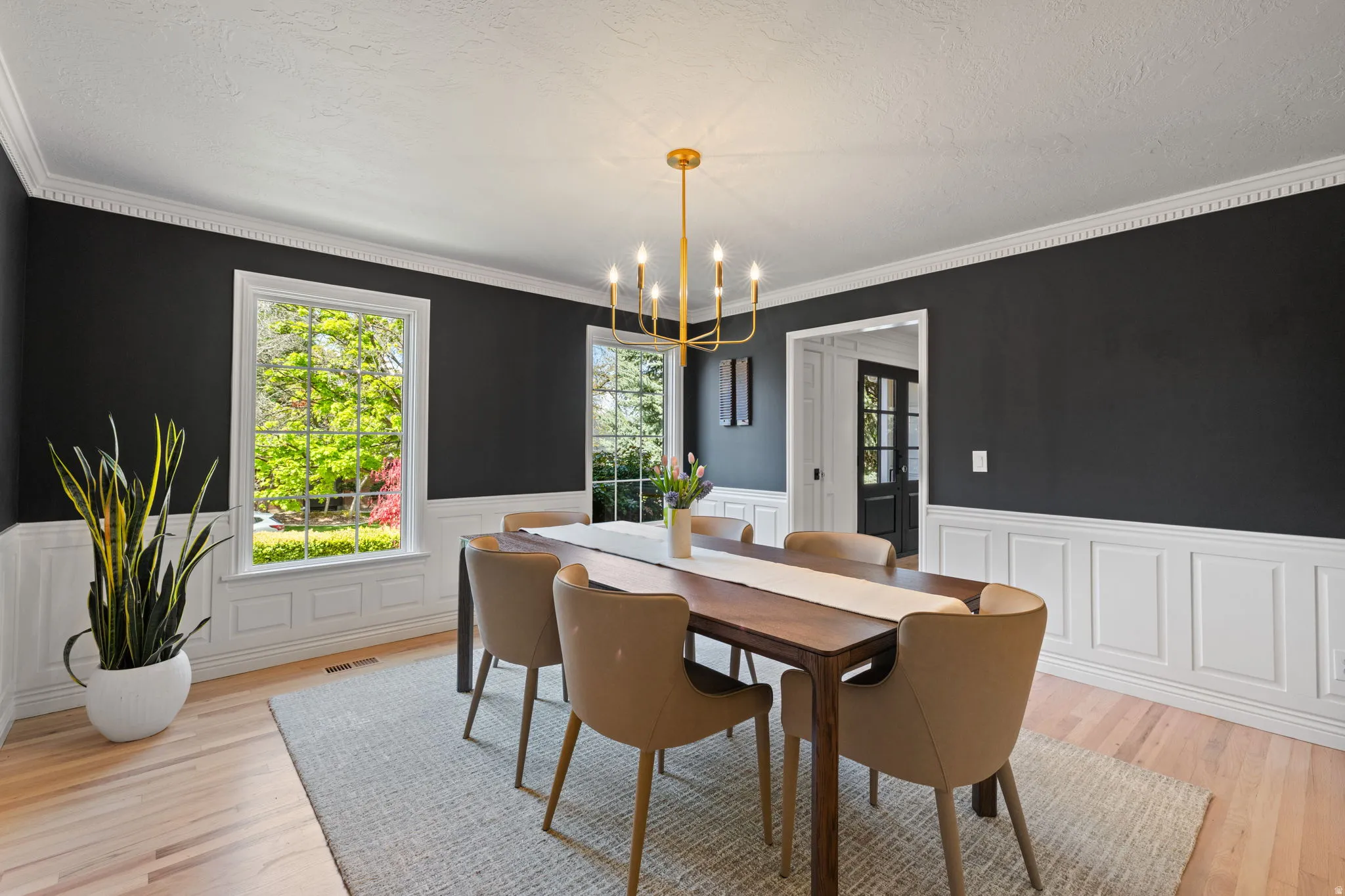 Dining room with a chandelier, wainscoting, light wood finished floors, crown molding, and a textured ceiling
