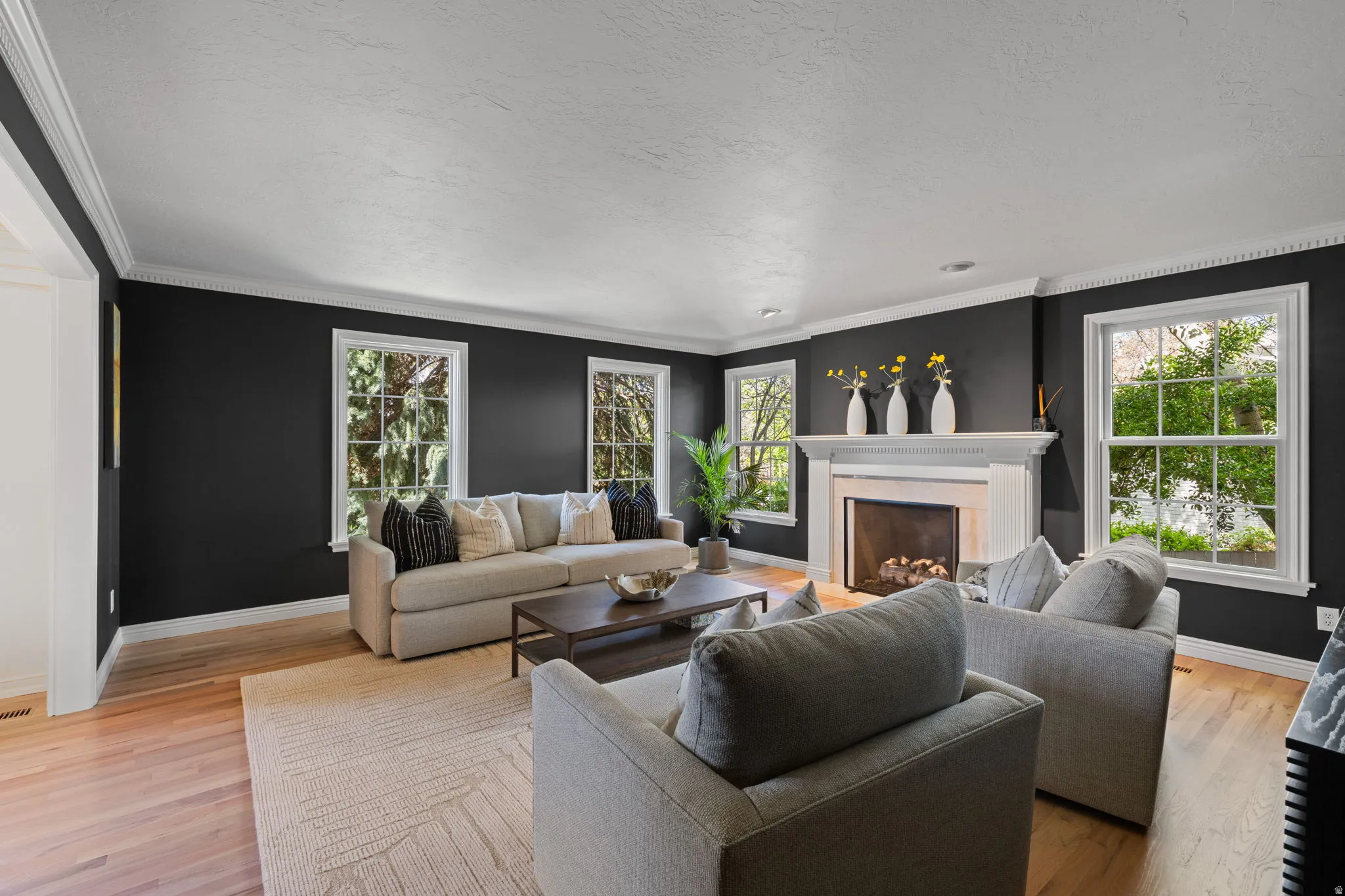 Living area featuring plenty of natural light, light wood-style flooring, a fireplace, crown molding, and a textured ceiling