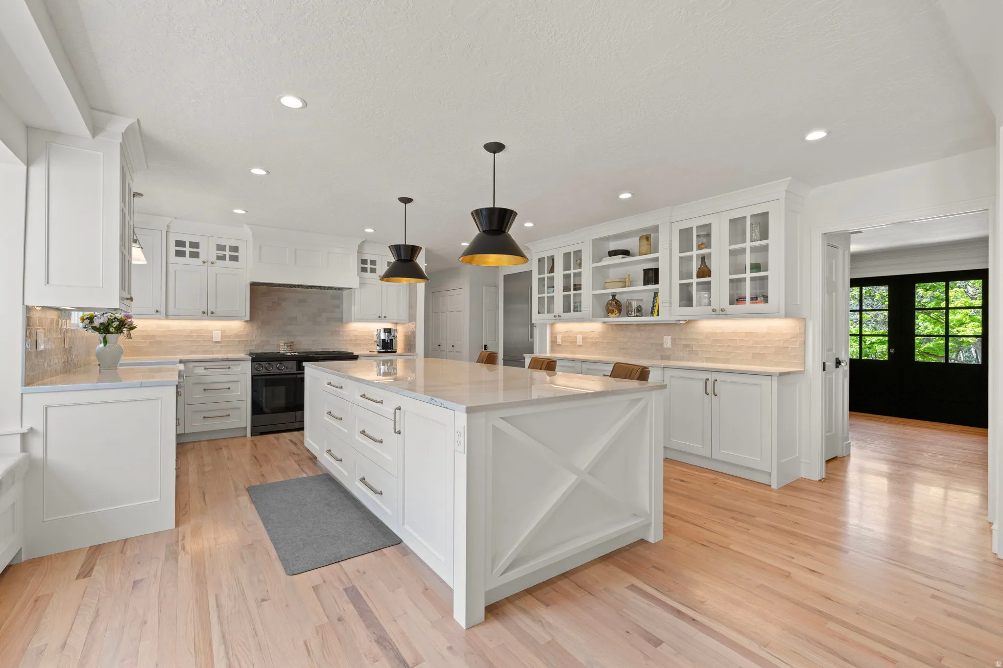 Kitchen with glass fronted cabinets, decorative light fixtures, and light stone counters