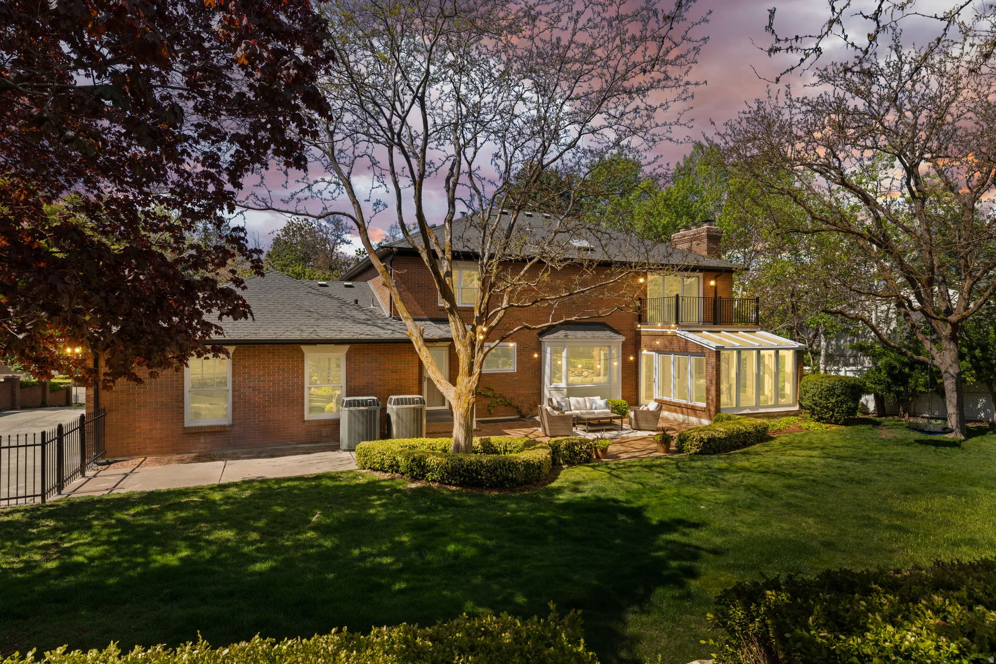 Back of house at dusk with brick siding, a sunroom, a patio area, and a chimney