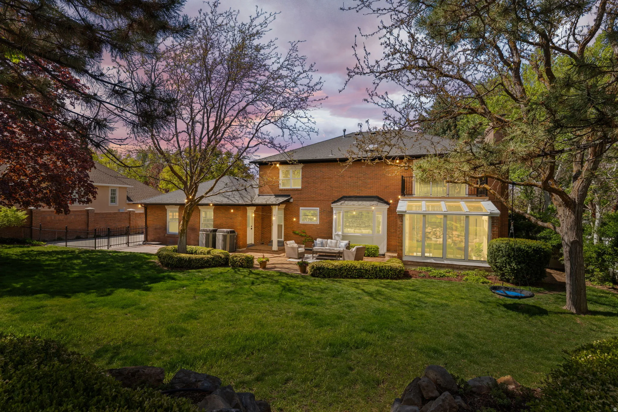 Back of property at dusk featuring brick siding, a patio area, outdoor furniture, and a sunroom