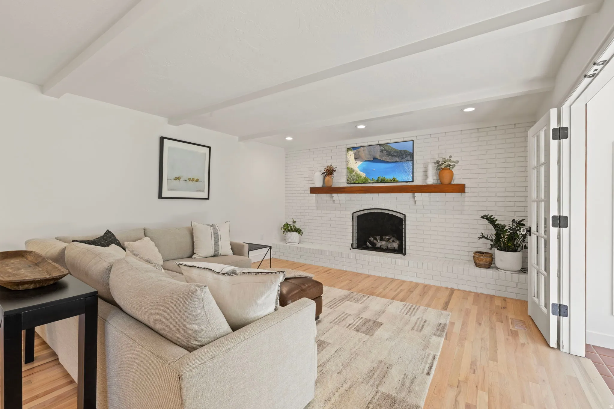 Living area with brick wall, a brick fireplace, beamed ceiling, light wood-style floors, and recessed lighting