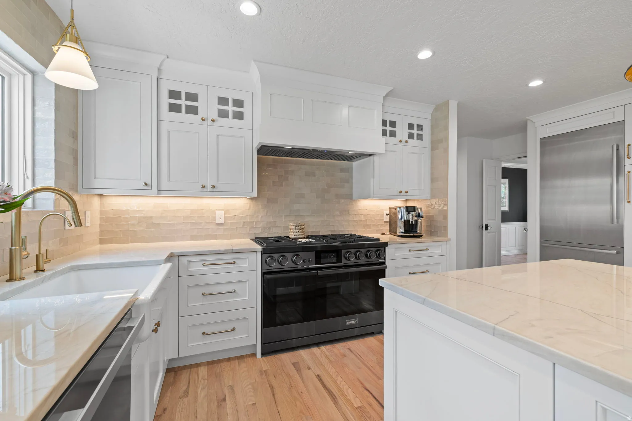 Kitchen with white cabinetry, premium appliances, glass fronted cabinets, and tasteful backsplash