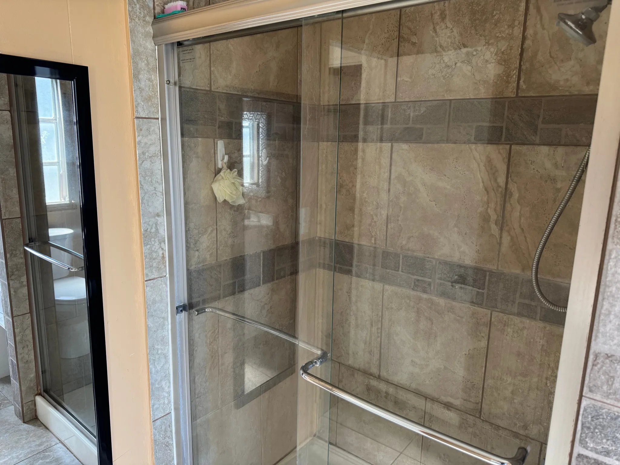 Glass-enclosed shower featuring large format tile walls with a decorative accent band and a handheld shower fixture