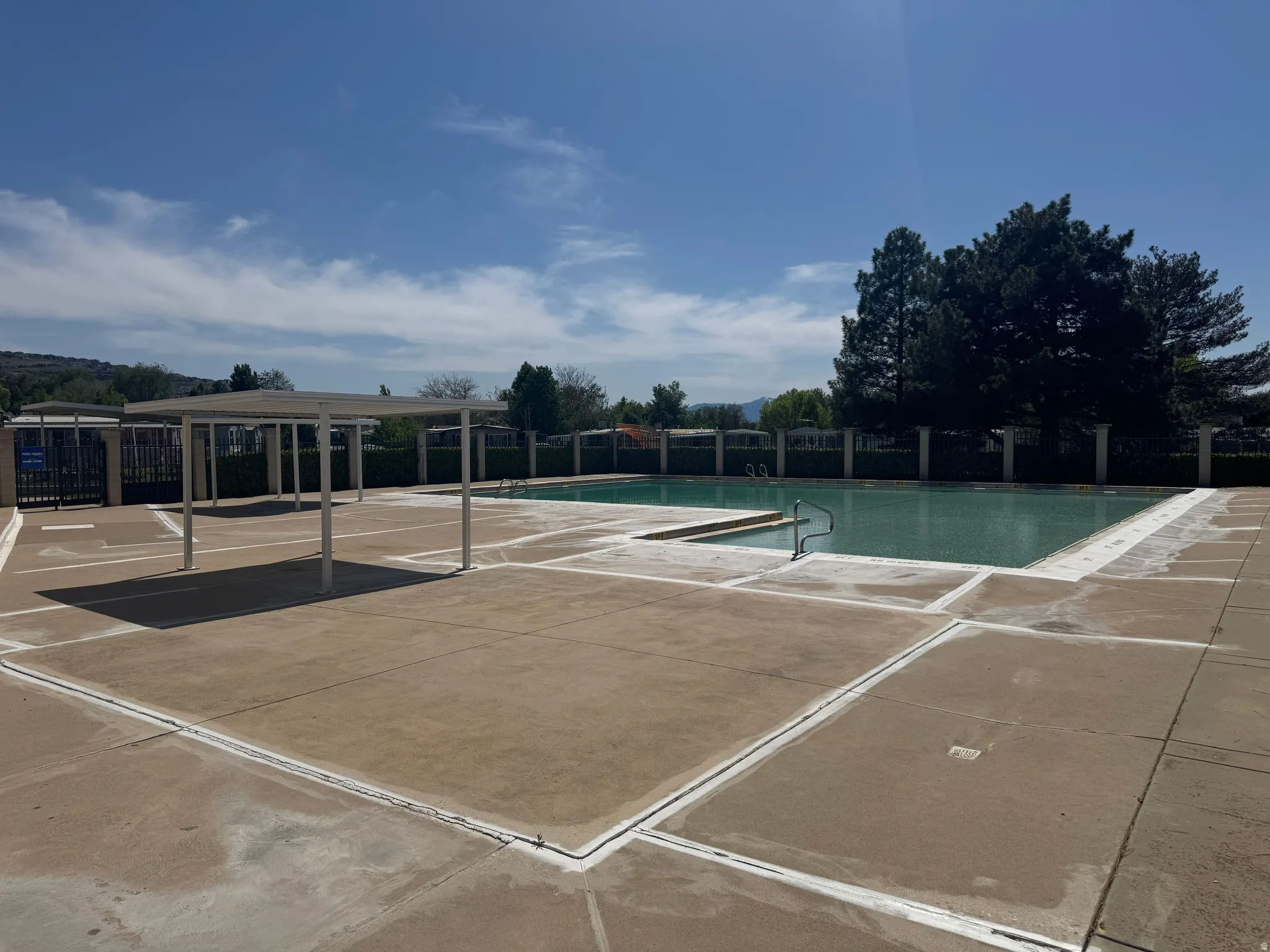 Expansive outdoor pool area featuring two distinct swimming pools, a gated perimeter, concrete decking, and a shade structure