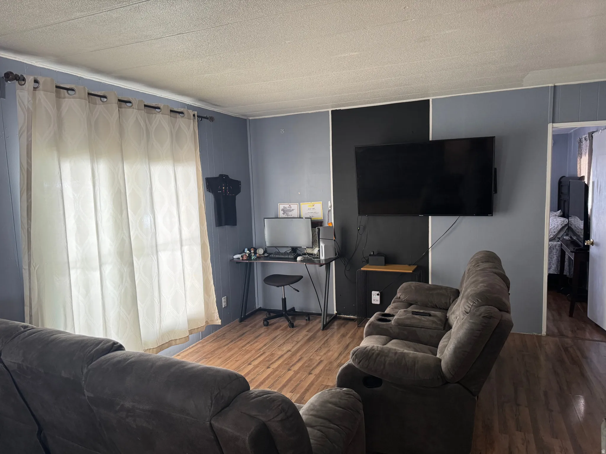Living area featuring wood-finish flooring, a full-wall accent panel, and a wall-mounted television