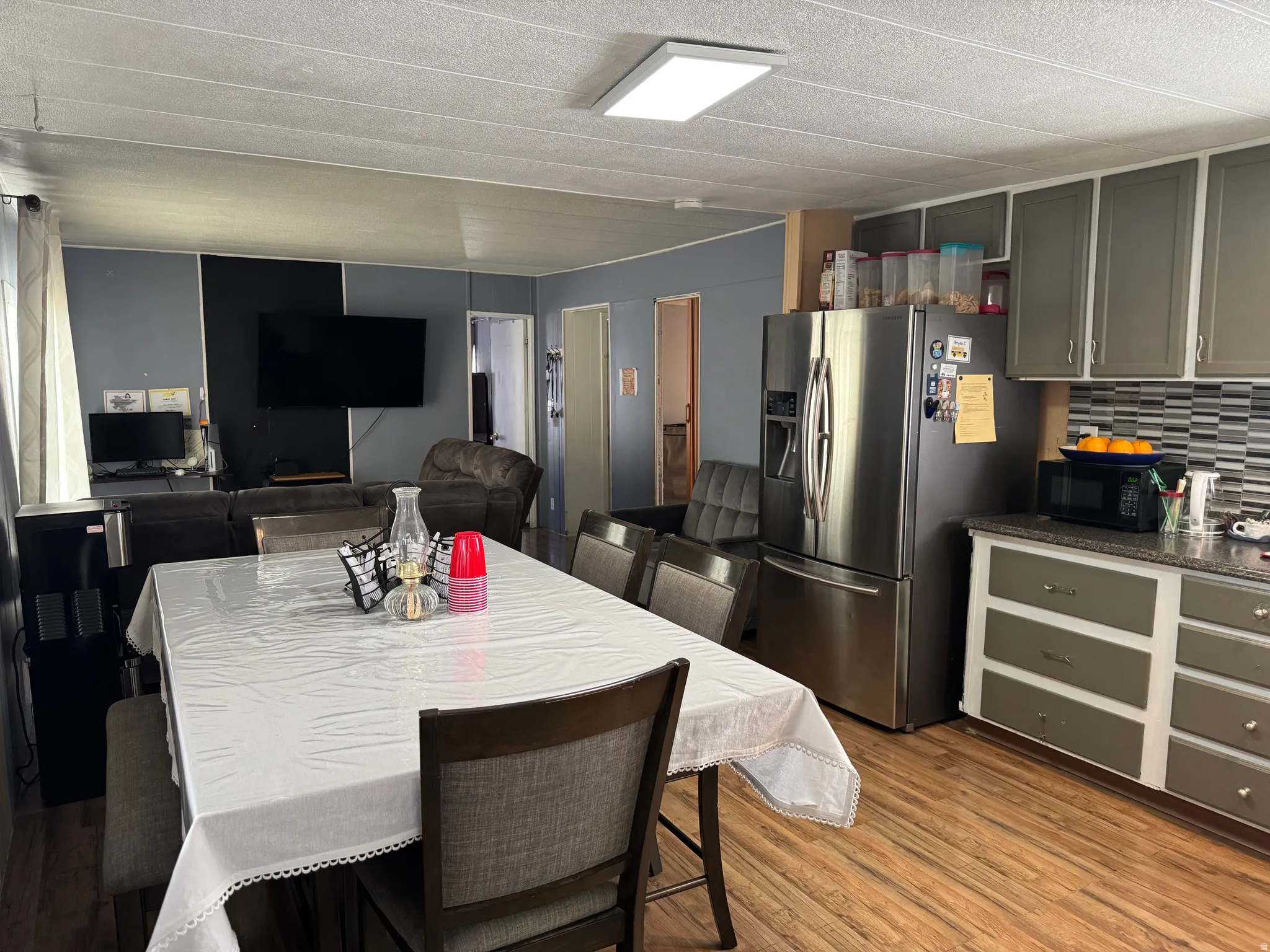 Open-concept kitchen and dining area featuring wood-finish flooring, gray cabinetry with white framing, and a stainless steel refrigerator