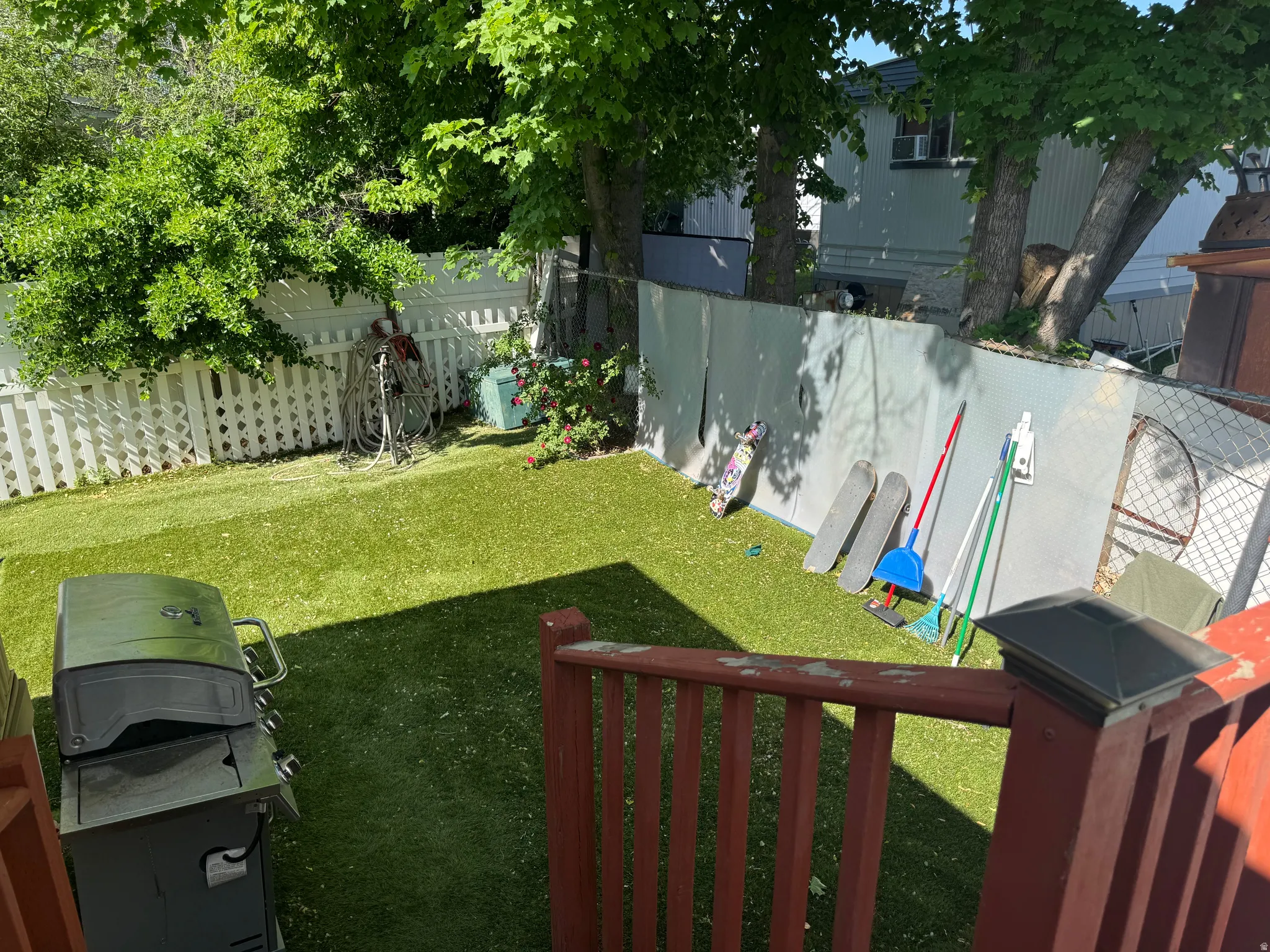 Expansive backyard featuring artificial turf, mature trees, and a white picket fence