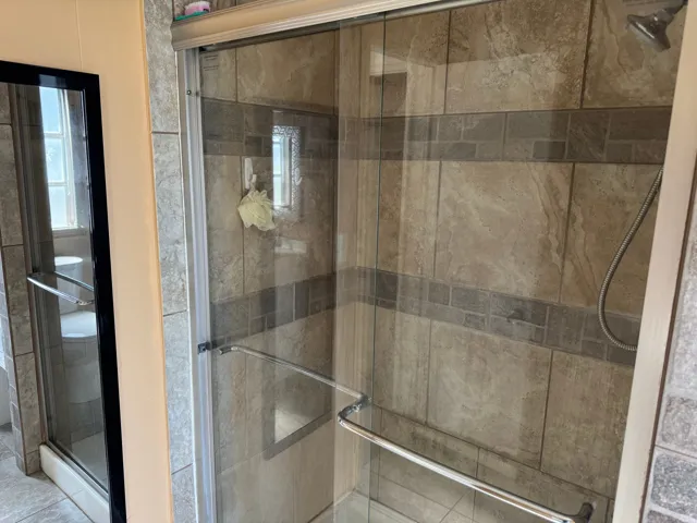 Glass-enclosed shower featuring large format tile walls with a decorative accent band and a handheld shower fixture