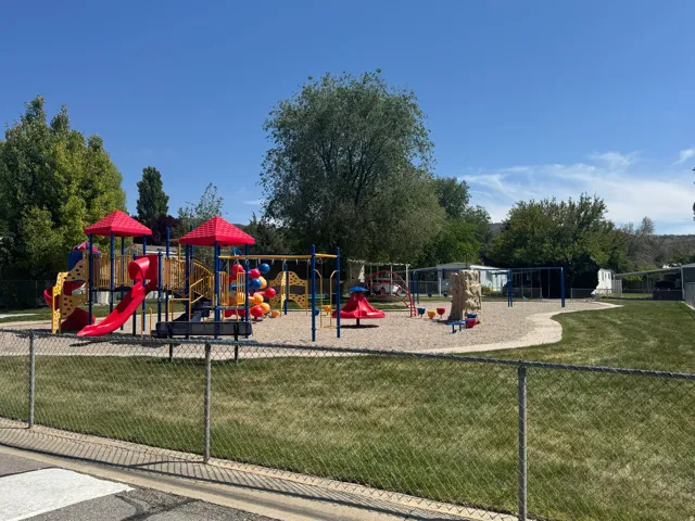 Community playground featuring a multi-level play structure with red slides and colorful accents, a rock climbing feature, and a swing set