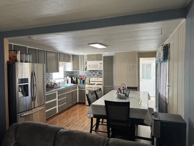 Kitchen and dining area featuring wood-finish flooring, gray cabinetry, a tiled backsplash, and stainless steel appliances