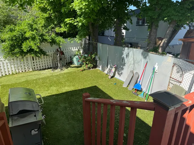 Expansive backyard featuring artificial turf, mature trees, and a white picket fence