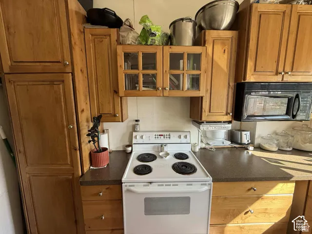 Kitchen featuring white range with electric stovetop, glass fronted cabinets, dark countertops, black microwave, and wood finish cabinets